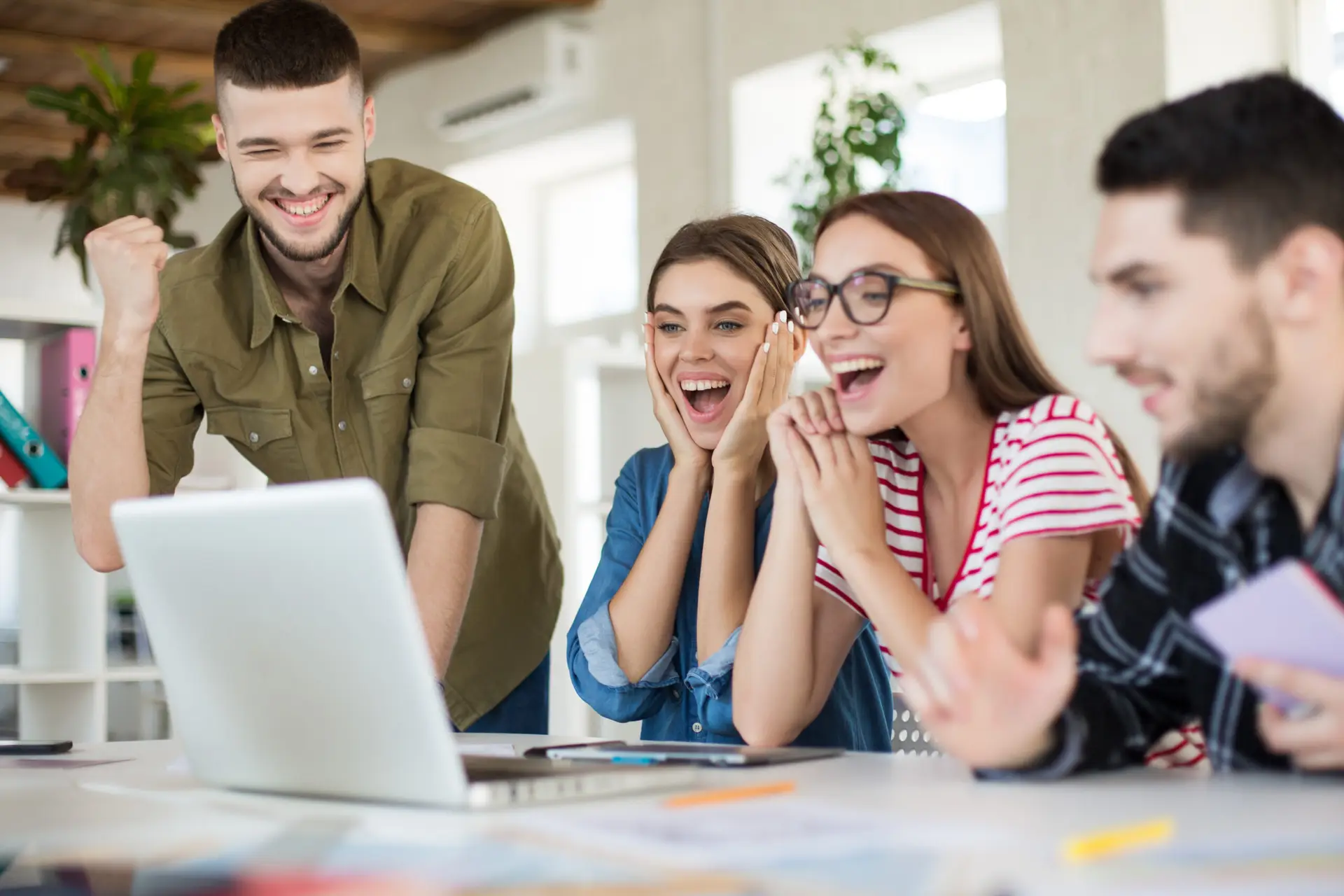 Young joyful business people happily working on laptop together. Group of smiling men and women spending time in modern cozy office